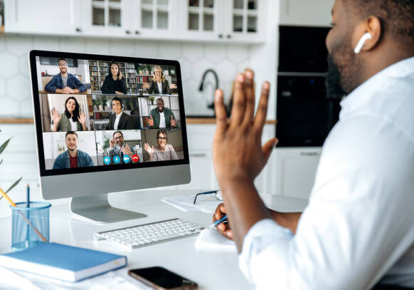 24-04 Video call, online conference. Over shoulder view of african american man at computer screen with multinational group of successful business people, virtual business meeting, work from home concept